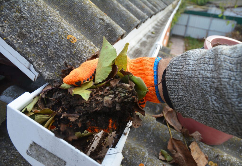 Man cleans dirt and leaves from roof guttering